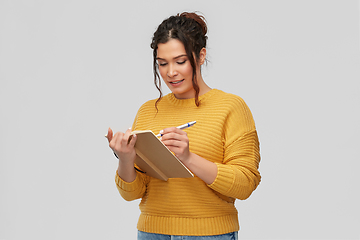 Image showing happy young woman writing to diary or notebook