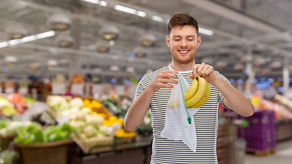 Image showing smiling man putting bananas into reusable net bag