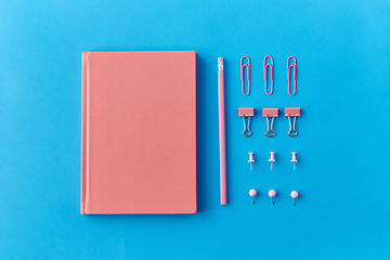 Image showing pink notebook, pins, clips and pencil on blue