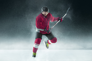 Image showing Male hockey player with the stick on ice court and dark background