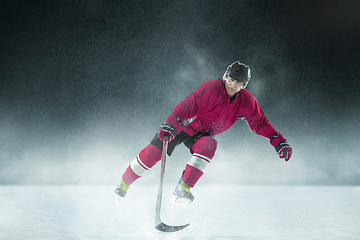 Image showing Male hockey player with the stick on ice court and dark background