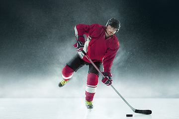 Image showing Male hockey player with the stick on ice court and dark background