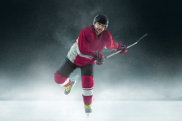 Image showing Male hockey player with the stick on ice court and dark background