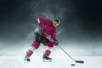 Image showing Male hockey player with the stick on ice court and dark background