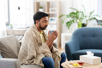 Image showing sick young man in blanket drinking hot tea at home