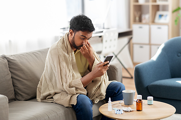 Image showing sick young man in blanket with smartphone at home