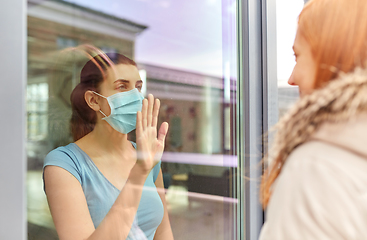Image showing ill woman in mask looking at friend through window