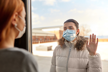 Image showing woman in mask looking to friend through window