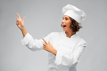 Image showing smiling female chef in toque pointing finger up