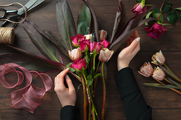 Image showing Florist at work: woman making fashion modern bouquet of different flowers on wooden background