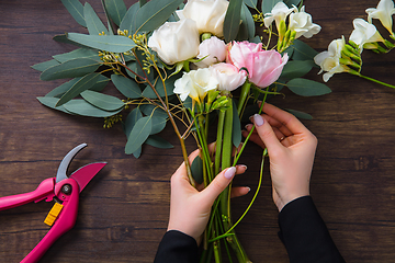 Image showing Florist at work: woman making fashion modern bouquet of different flowers on wooden background