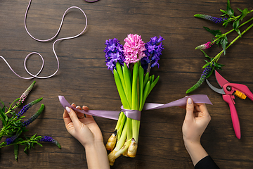 Image showing Florist at work: woman making fashion modern bouquet of different flowers on wooden background