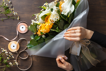 Image showing Florist at work: woman making fashion modern bouquet of different flowers on wooden background