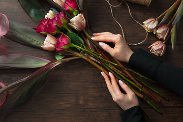 Image showing Florist at work: woman making fashion modern bouquet of different flowers on wooden background