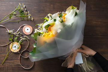 Image showing Florist at work: woman making fashion modern bouquet of different flowers on wooden background