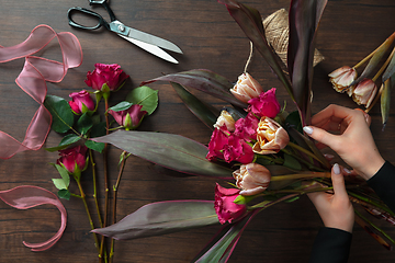 Image showing Florist at work: woman making fashion modern bouquet of different flowers on wooden background