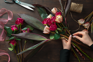 Image showing Florist at work: woman making fashion modern bouquet of different flowers on wooden background