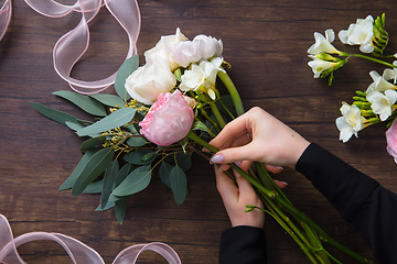 Image showing Florist at work: woman making fashion modern bouquet of different flowers on wooden background