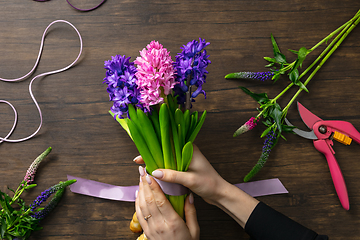 Image showing Florist at work: woman making fashion modern bouquet of different flowers on wooden background