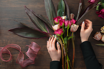 Image showing Florist at work: woman making fashion modern bouquet of different flowers on wooden background