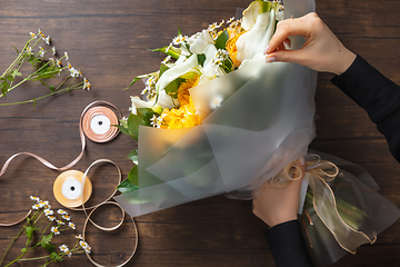 Image showing Florist at work: woman making fashion modern bouquet of different flowers on wooden background