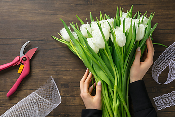 Image showing Florist at work: woman making fashion modern bouquet of different flowers on wooden background