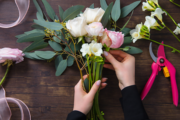 Image showing Florist at work: woman making fashion modern bouquet of different flowers on wooden background