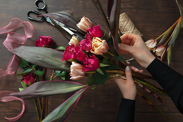 Image showing Florist at work: woman making fashion modern bouquet of different flowers on wooden background