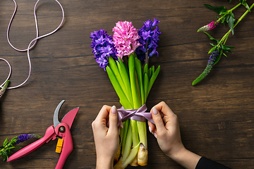 Image showing Florist at work: woman making fashion modern bouquet of different flowers on wooden background