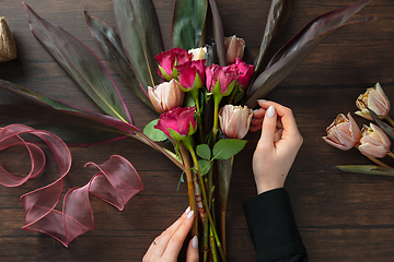 Image showing Florist at work: woman making fashion modern bouquet of different flowers on wooden background