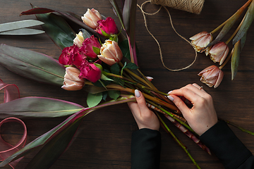 Image showing Florist at work: woman making fashion modern bouquet of different flowers on wooden background