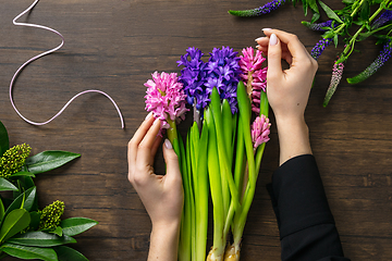 Image showing Florist at work: woman making fashion modern bouquet of different flowers on wooden background