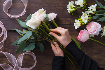 Image showing Florist at work: woman making fashion modern bouquet of different flowers on wooden background