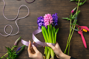 Image showing Florist at work: woman making fashion modern bouquet of different flowers on wooden background