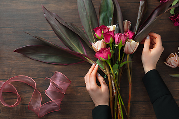 Image showing Florist at work: woman making fashion modern bouquet of different flowers on wooden background