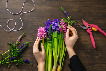 Image showing Florist at work: woman making fashion modern bouquet of different flowers on wooden background