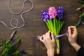 Image showing Florist at work: woman making fashion modern bouquet of different flowers on wooden background