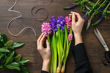 Image showing Florist at work: woman making fashion modern bouquet of different flowers on wooden background