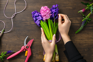 Image showing Florist at work: woman making fashion modern bouquet of different flowers on wooden background