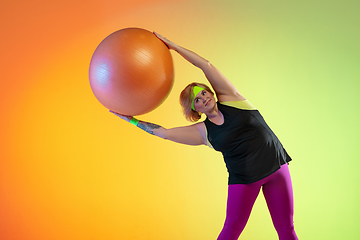 Image showing Young caucasian plus size female model\'s training on gradient orange background