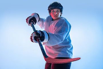 Image showing Young male hockey player with the stick on ice court and white background in neon light