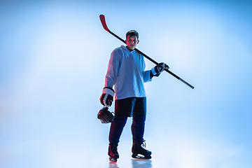 Image showing Young male hockey player with the stick on ice court and white background in neon light