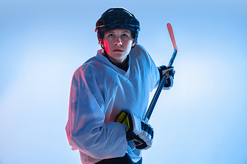 Image showing Young male hockey player with the stick on ice court and white background in neon light