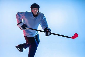 Image showing Young male hockey player with the stick on ice court and white background in neon light