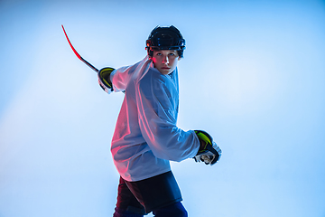 Image showing Young male hockey player with the stick on ice court and white background in neon light