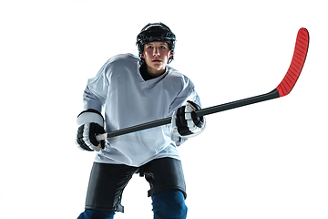 Image showing Young male hockey player with the stick on ice court and white background