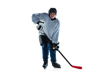 Image showing Young male hockey player with the stick on ice court and white background