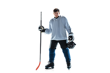 Image showing Young male hockey player with the stick on ice court and white background