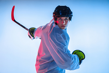Image showing Young male hockey player with the stick on ice court and white background in neon light