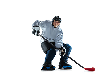 Image showing Young male hockey player with the stick on ice court and white background